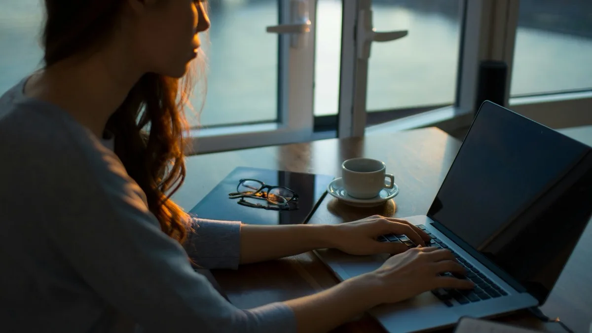 Kobieta korzystająca z laptopa przy stoliku obok okna